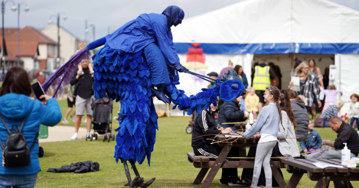Child smiling at street performer dressed a big blue bird at Seaham Food Festival.